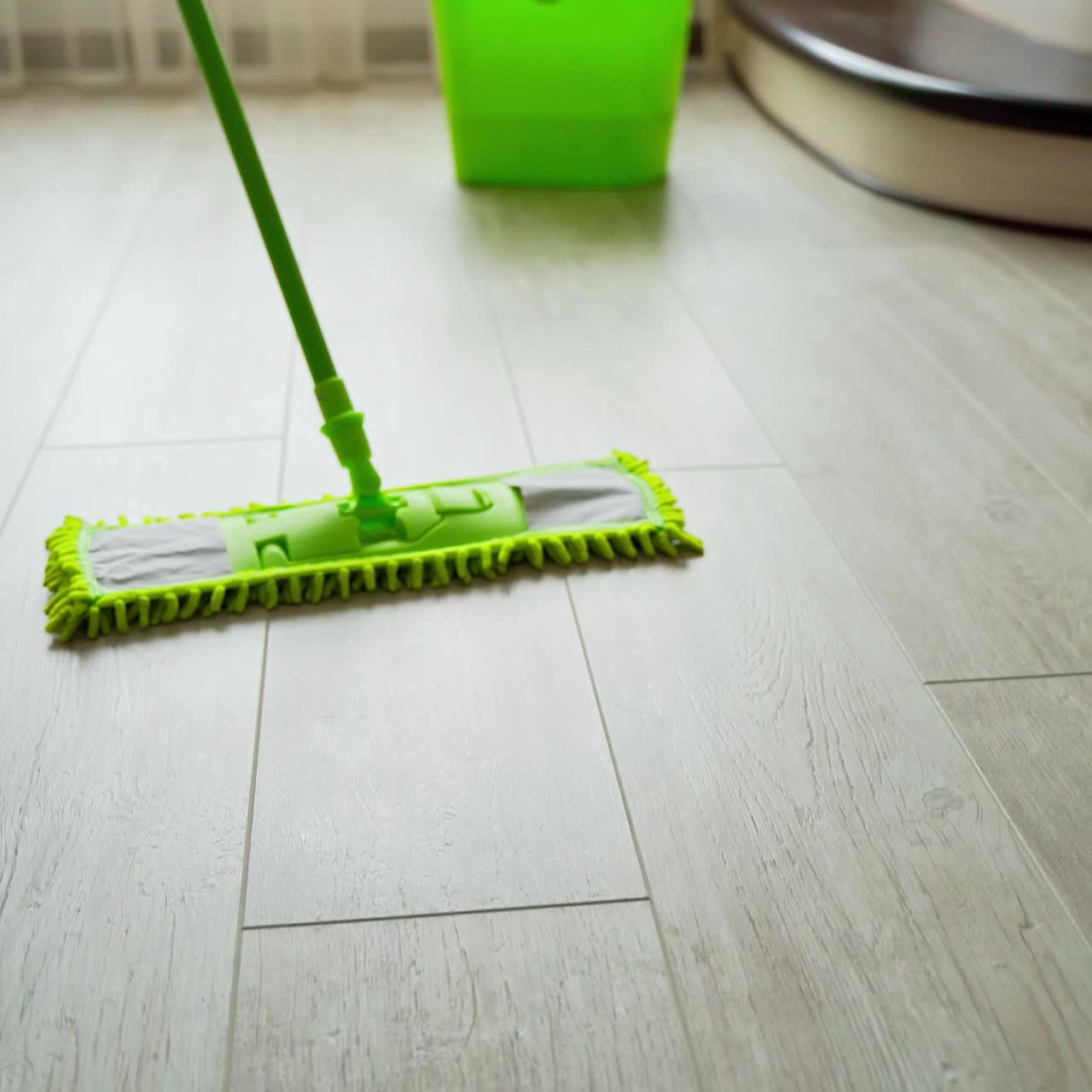 Microfiber wet mop moving around the floor at home. Person in slippers mopping the floor with a green brush. Housework. Close-up.