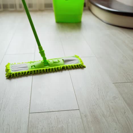 microfiber wet mop moving around the floor at home. person in slippers mopping the floor with a green brush. housework. close-up.