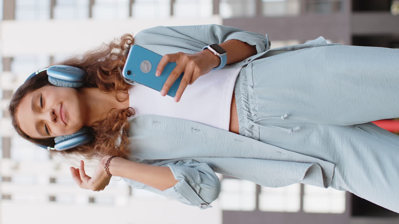 niña preadolescente feliz con auriculares inalámbricos eligiendo, escuchando música bailando al aire libre en la calle de la ciudad