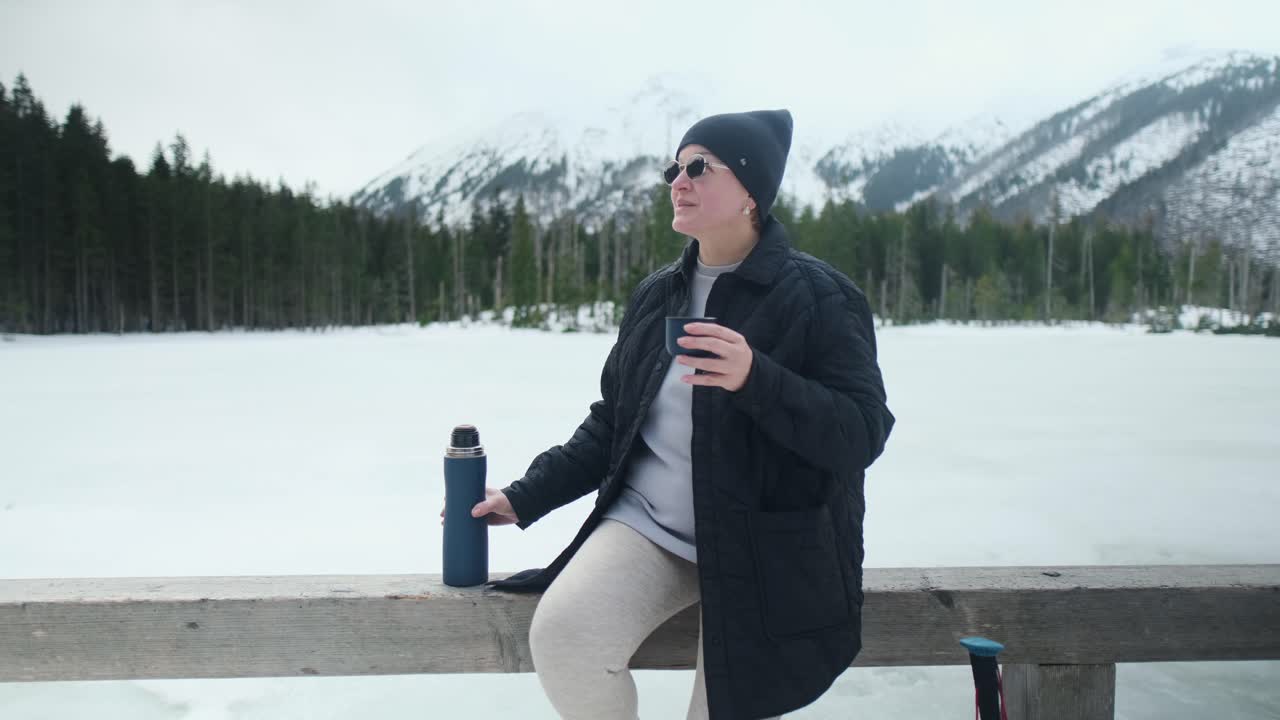 Woman enjoying a hot drink by a frozen lake in winter mountains