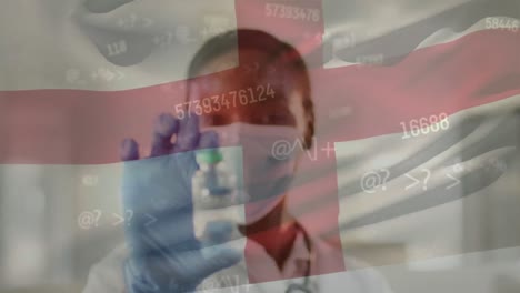 Animation-of-numbers-and-england-flag-over-biracial-female-doctor-in-face-mask-holding-vaccine