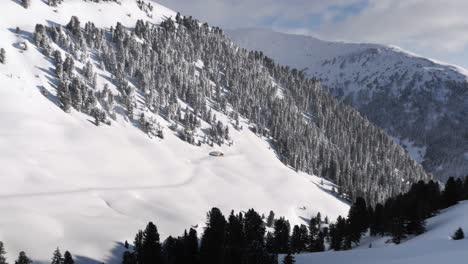 Isolated-snow-covered-chalet-in-snow-covered-mountains-with-trees-and-blue-sky,-zooming-out