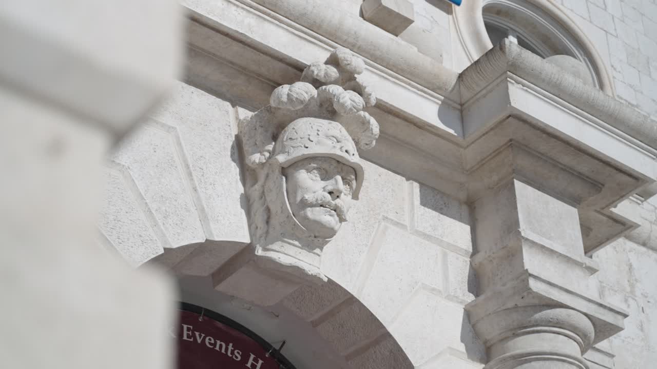 Revealing closeup on a faced head sculpture in Dubrovnik Croatia old town above an entrace looking like a general with a helmet and feathers on top