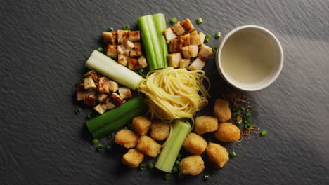 gourmet asian food arrangement with eel, noodles, and celery on a dark surface