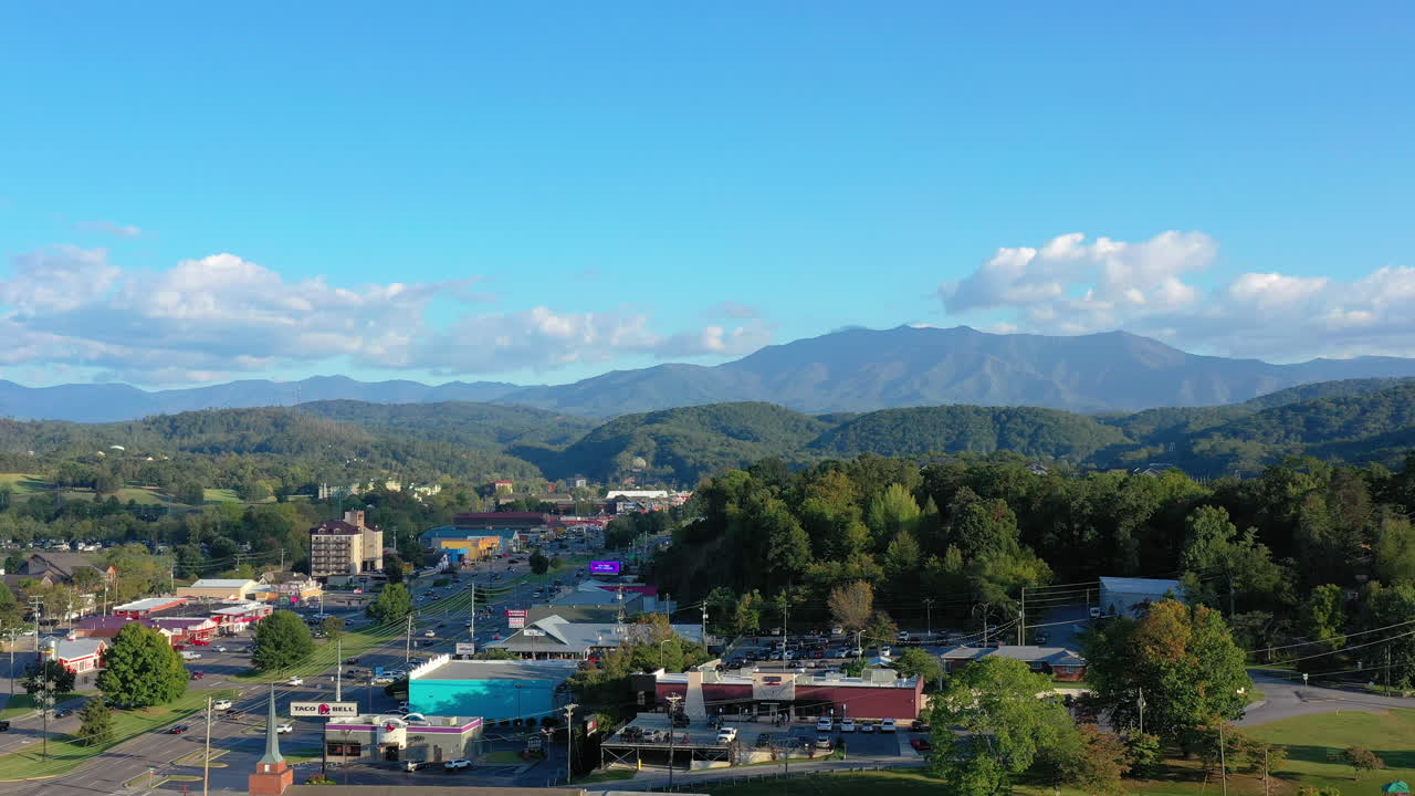 Aerial view of a lively Tennessee town framed by the Great Smoky Mountains—rolling hills, scattered clouds, and sunlit streets capture the charm and energy of the region