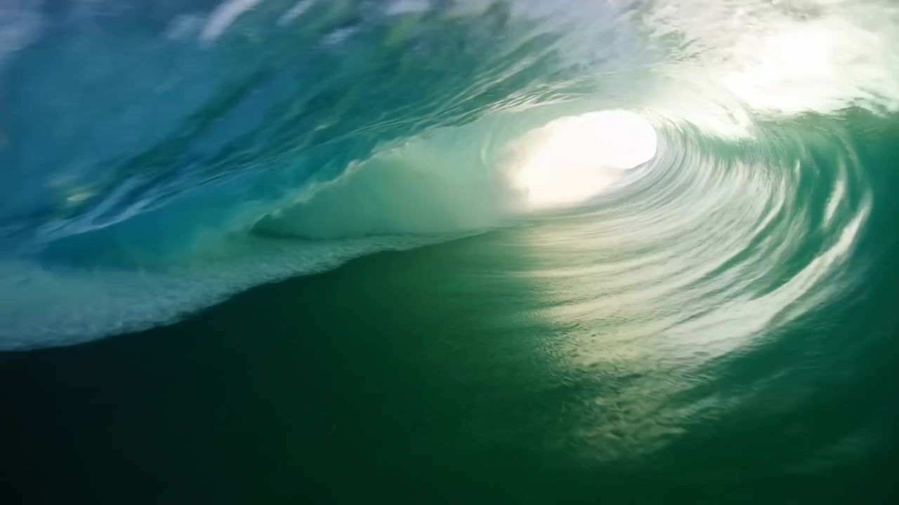 Low water-level interior view of breaking ocean wave showing fully formed barrel and curling lip with bright circular sunlight opening