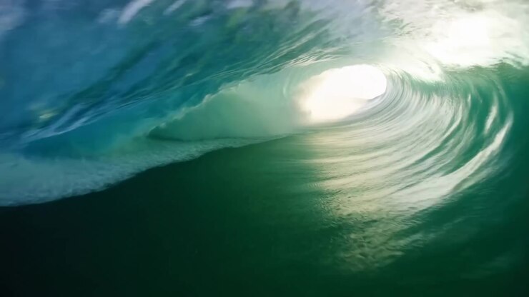 Low water-level interior view of breaking ocean wave showing fully formed barrel and curling lip with bright circular sunlight opening