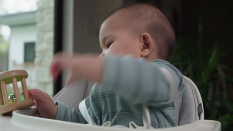 cute asian baby in high chair playing and eating bell rattle toy