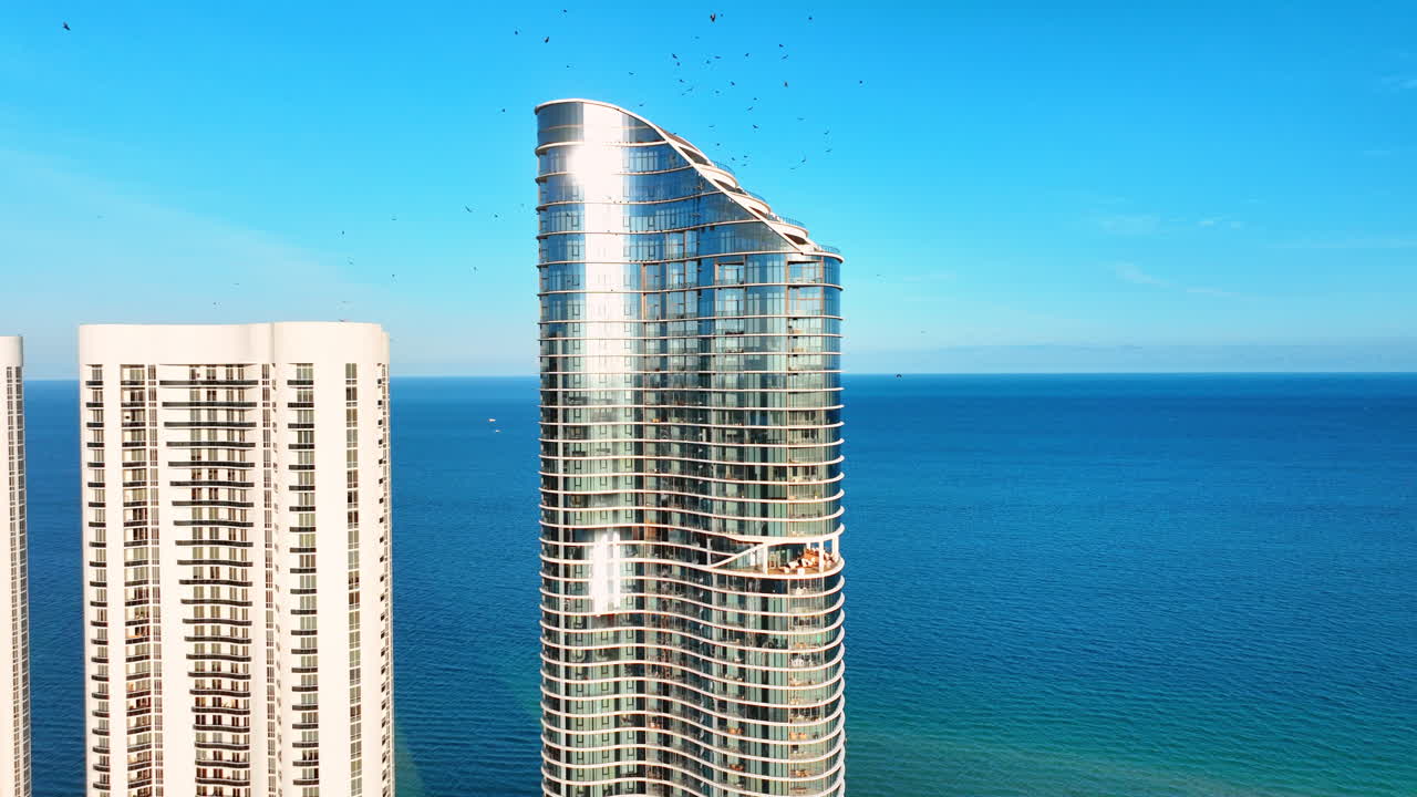 Dettaglio di un moderno grattacielo con vetro riflettente su uno sfondo di mare blu limpido. Primo piano della facciata curva di un grattacielo in vetro. Hotel sulla costa di Sunny Isles Beach.