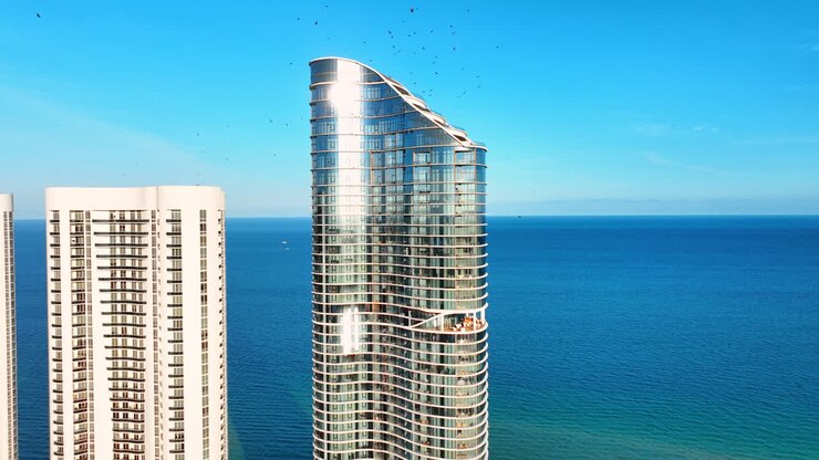 Dettaglio di un moderno grattacielo con vetro riflettente su uno sfondo di mare blu limpido. Primo piano della facciata curva di un grattacielo in vetro. Hotel sulla costa di Sunny Isles Beach.