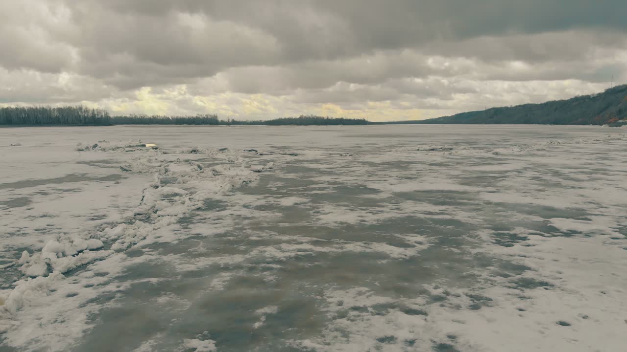흐린 하늘 아래 눈이 내리는 얼어붙은 강 위의 공중 움직임