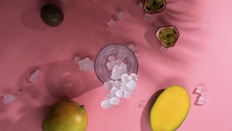 cubitos de hielo cayendo sobre la mesa de frutas con vaso de cóctel