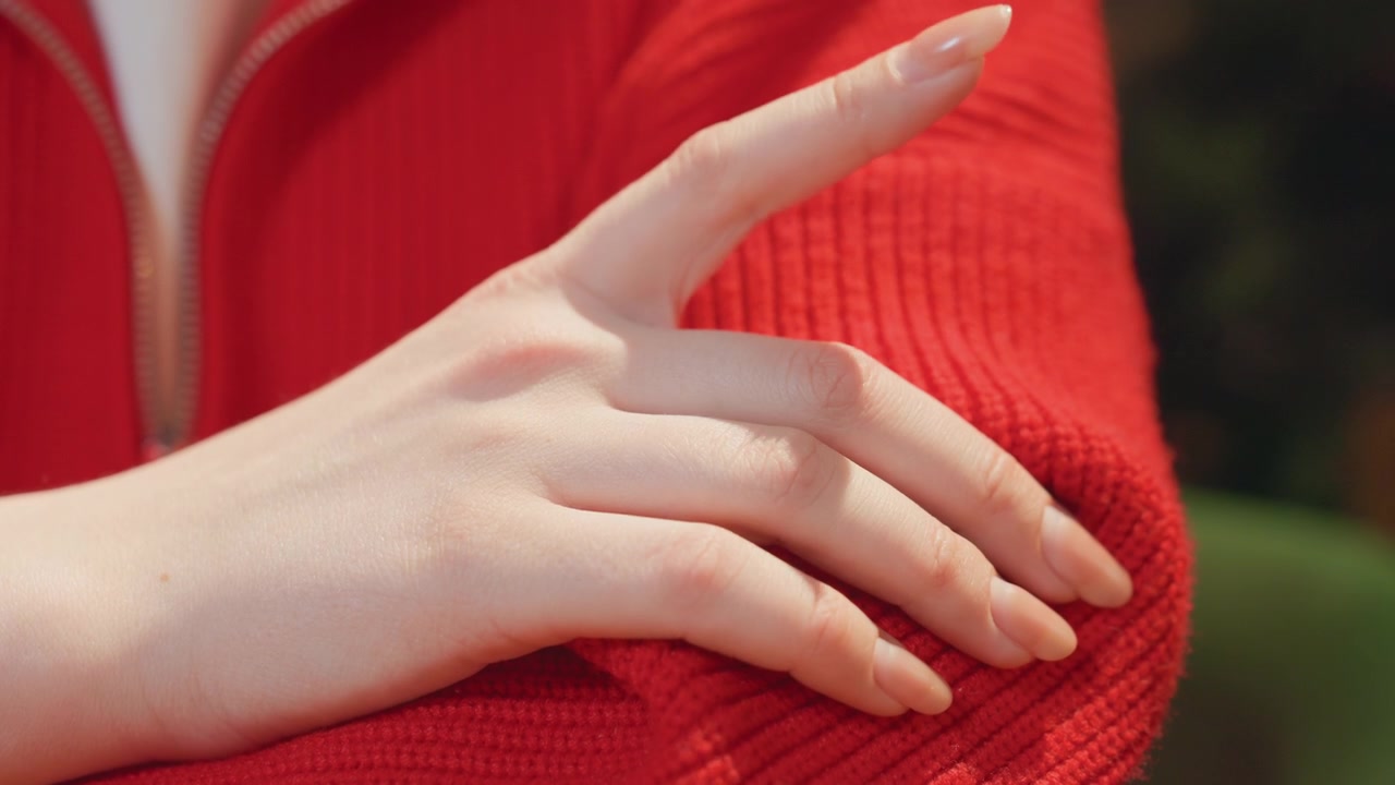 Close-up of a hand with natural nails resting on a red sweater