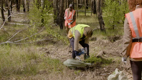 Caucasian-and-african-american-men-activists-using-a-shovel-and-a-rake-to-prepare-the-land-and-plant-trees-in-the-forest