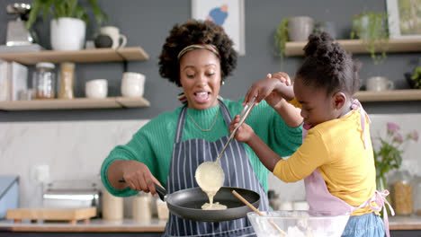 Happy-african-american-mother-and-daughter-frying-pancakes-in-kitchen,-slow-motion