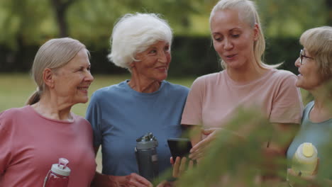 entrenadora femenina usando un teléfono inteligente y charlando con mujeres mayores en el parque