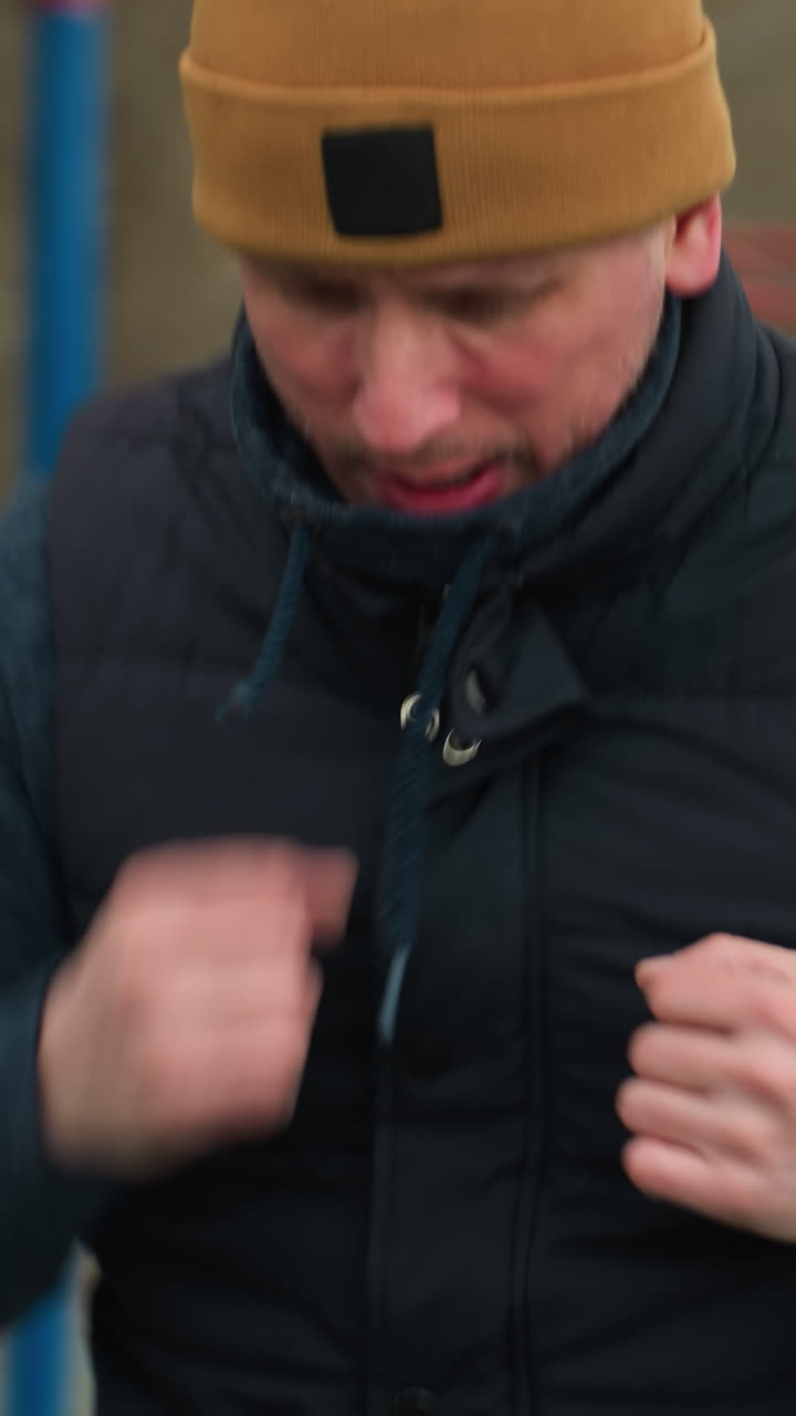 primer plano de un entrenador trabajando a un ritmo rápido, con un coche negro y un coche blanco moviéndose en direcciones opuestas a través de la carretera detrás de él, con árboles estériles en el fondo