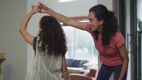 Glückliche-Gemischtrassige-Mutter-Und-Tochter-Tanzen-Im-Wohnzimmer