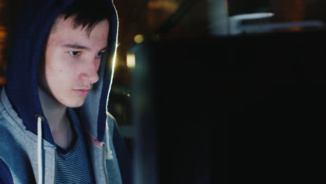 un adolescente encapuchado se sienta frente a un monitor de computadora en la oscuridad 1