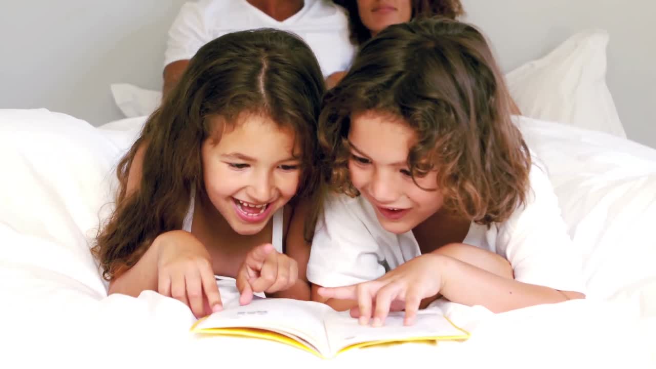 hermanos lindos leyendo un libro en la cama de sus padres
