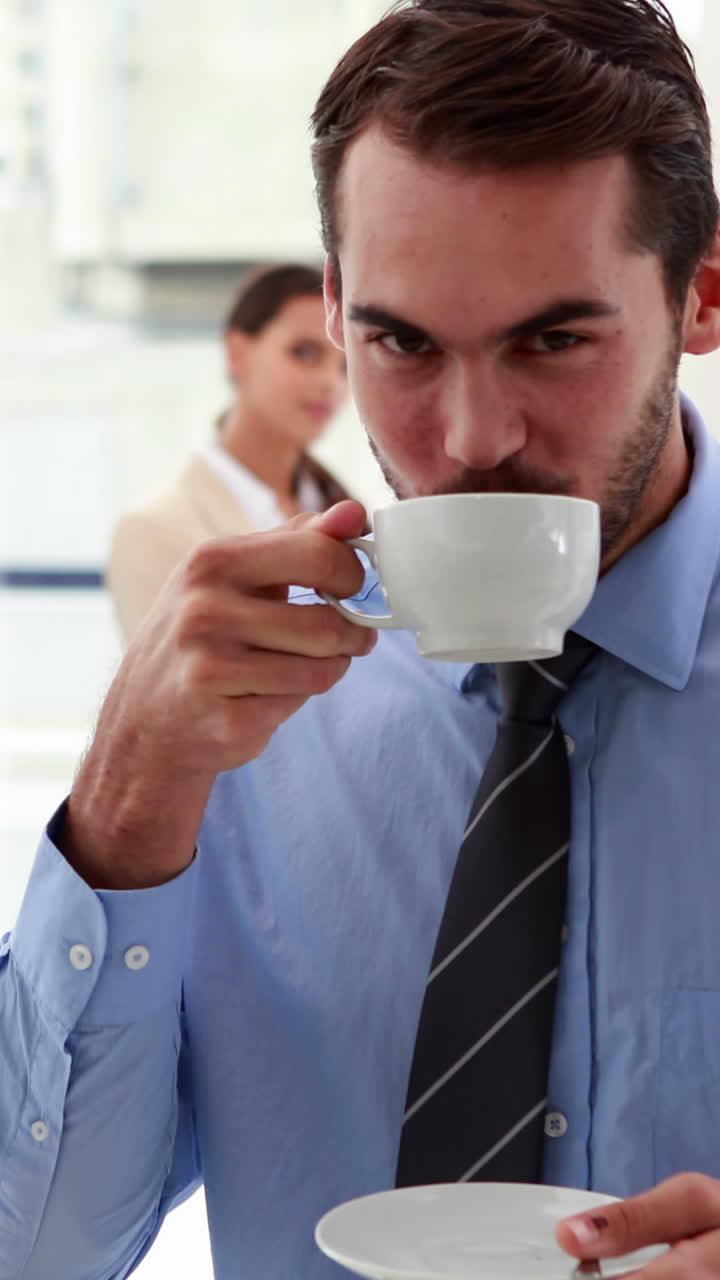 hombre de negocios de pie y bebiendo un café con colegas detrás