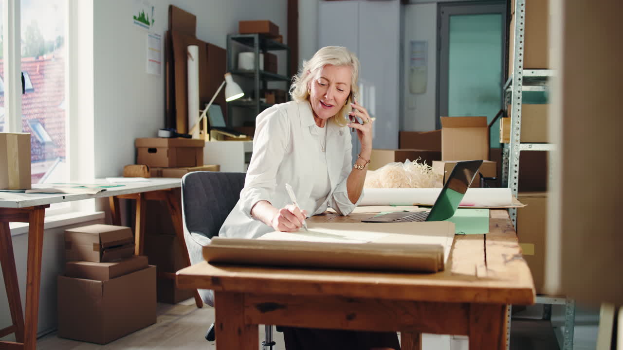 Senior Businesswoman Talking on Phone and Writing in Office