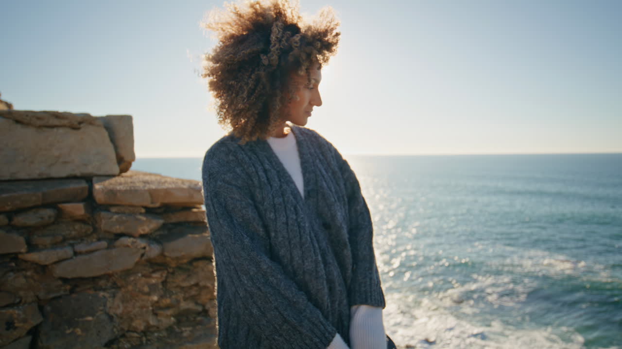 Curly model watching ocean at windy coast closeup. Tanned woman looking camera