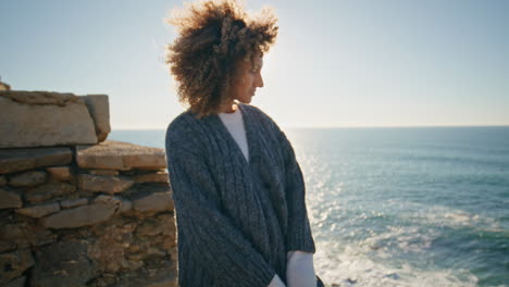 curly model watching ocean at windy coast closeup. tanned woman looking camera