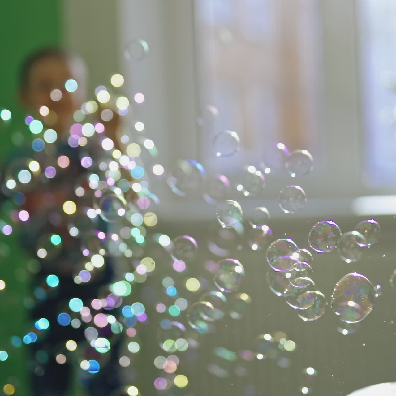 Many colorful bubbles flying in the room and a little boy playing with them. Joyful boy jumping happily and playing with soapy bubbles indoors. Soap bubbles show and a happy boy.