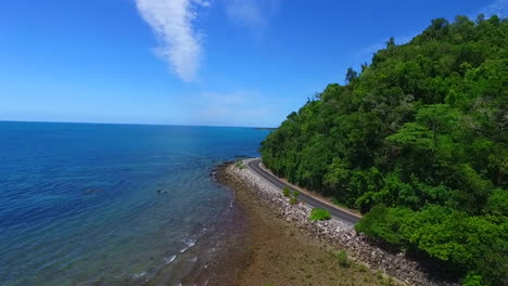 A-blue-car-travelling-along-a-tropical-coastal-road-next-to-the-ocean