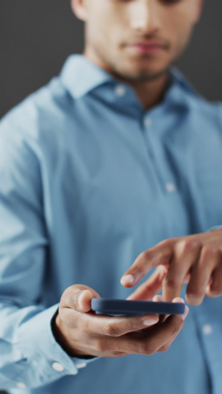 Vertical video of smiling biracial businessman using smartphone and holographic display, copy space