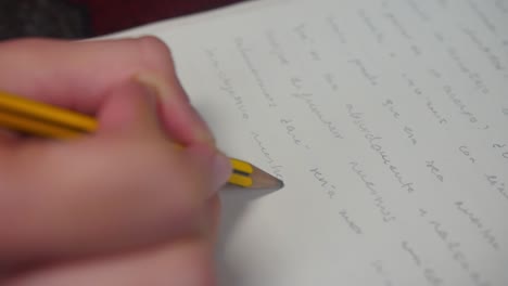 primer plano de manos escribiendo palabras en español con un lápiz en cámara lenta sobre una hoja blanca de papel