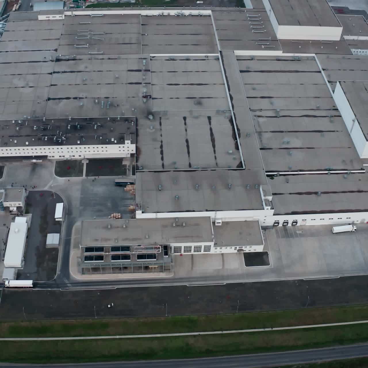 Large industrial complex. Exterior of production plant on field. Grey manufacturing with car parking. Motion camera to the left. Aerial view.