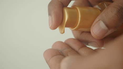 a man's hand is shown applying a liquid lotion from a gold pump bottle to his other hand.