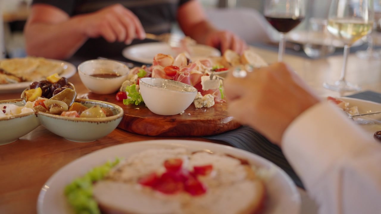 Close Up of People Eat Gourmet Food Table with Charcuterie Meat Board and Wine Glasses at Restaurant