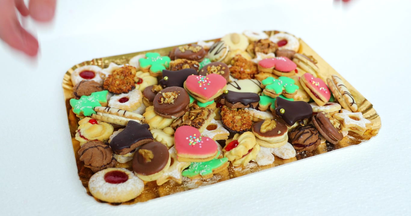 Hand that lifts up Christmas cookies, which is superimposed on a golden plate decorated and stacked wearing different color varieties and sizes in slow motion capture at 120fps