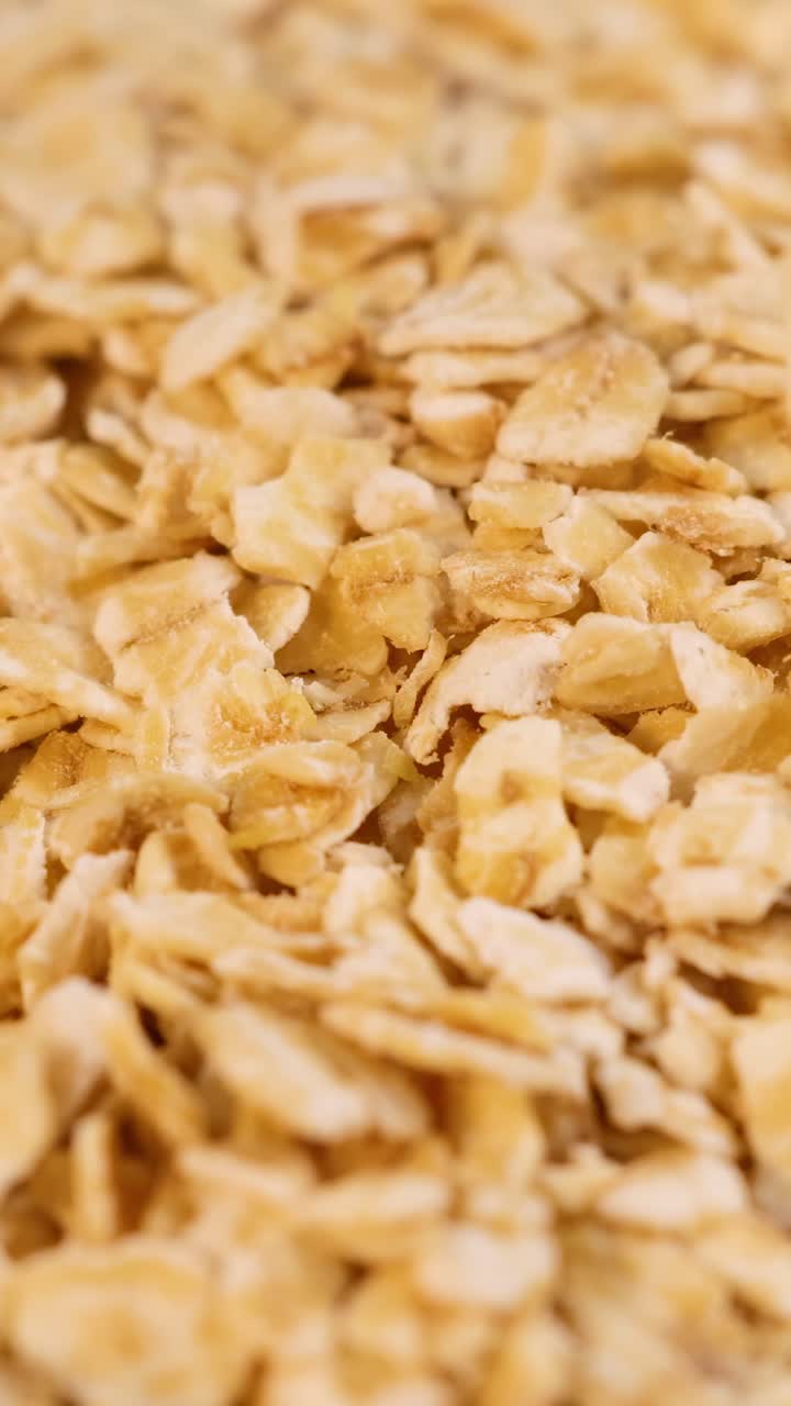 I fiocchi d'avena cadono delicatamente, creando una superficie dorata e testurizzata. L'illuminazione soffusa esalta i dettagli naturali della grana.
