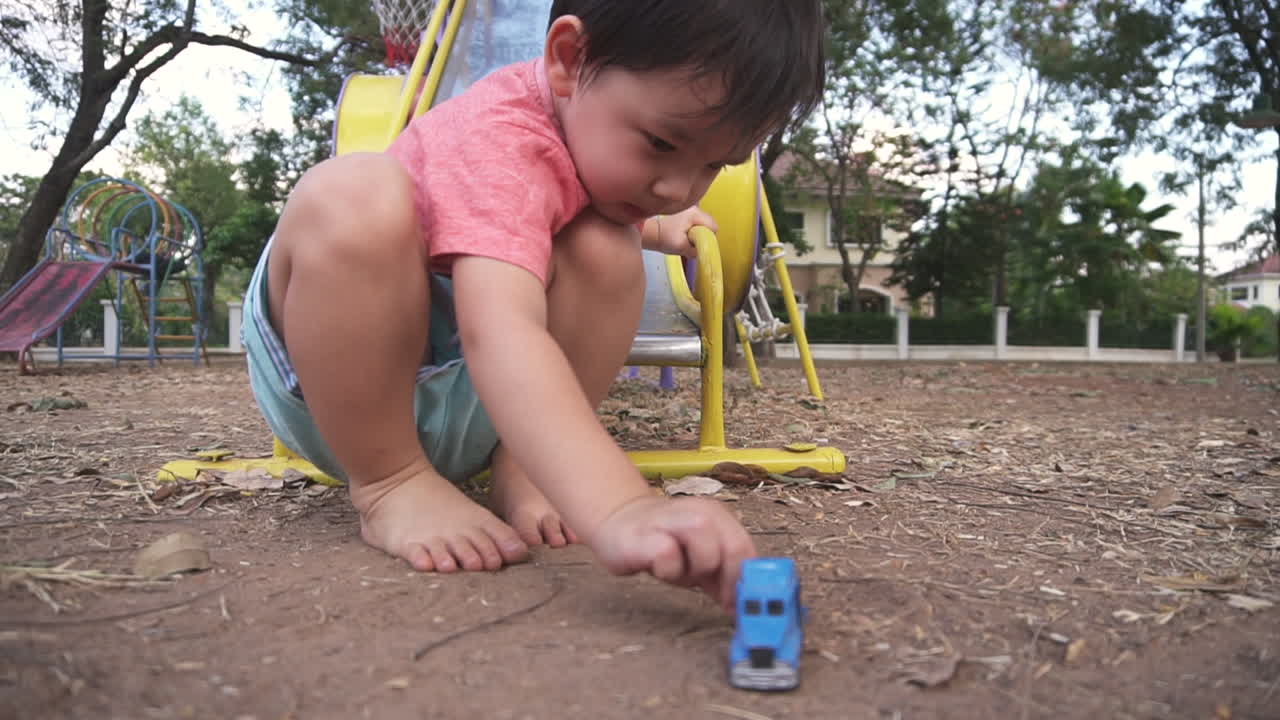 Close up shot of a happy  East Asian boy kid having fun playing at a park outdoors with toy cars