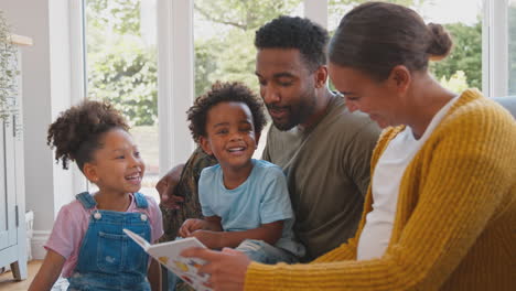 army family with pregnant mother sitting on floor in lounge at home reading book together