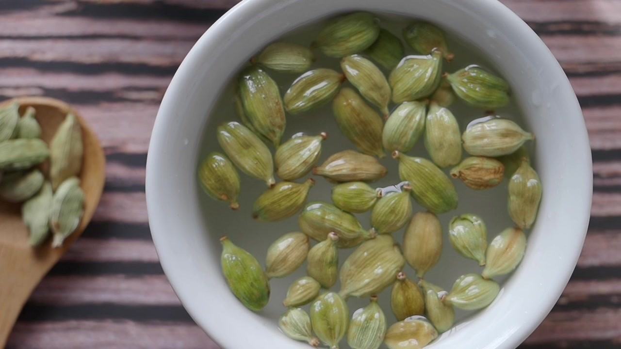 Aggiungere baccelli di cardamomo verde all'acqua in una ciotola bianca