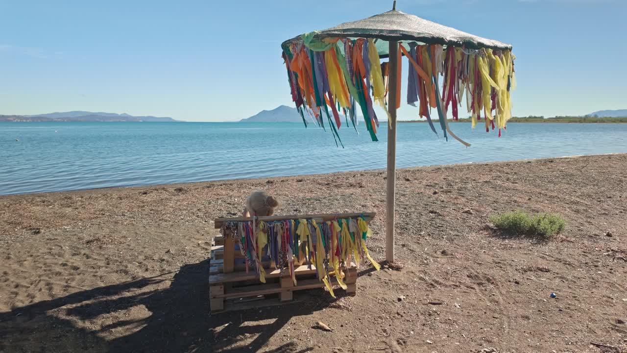 Woman Relaxing on a Beach Bench under a Colorful Ribbon Decorated Umbrella