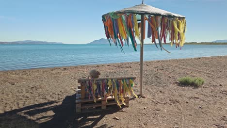 woman relaxing on a beach bench under a colorful ribbon decorated umbrella