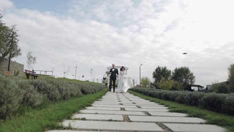 Recién-Casados,-Hermosa-Novia-Y-Novio-Caucásicos-Corriendo-Por-El-Camino-Durante-La-Ceremonia-De-Boda-En-El-Parque