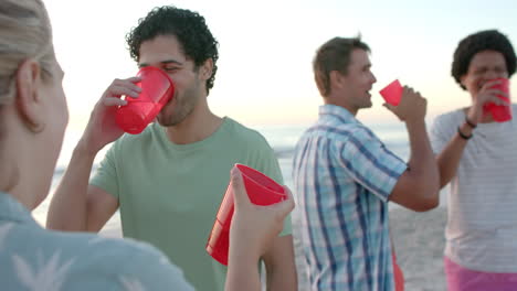 young caucasian woman and diverse group of men enjoy drinks on the beach at a party