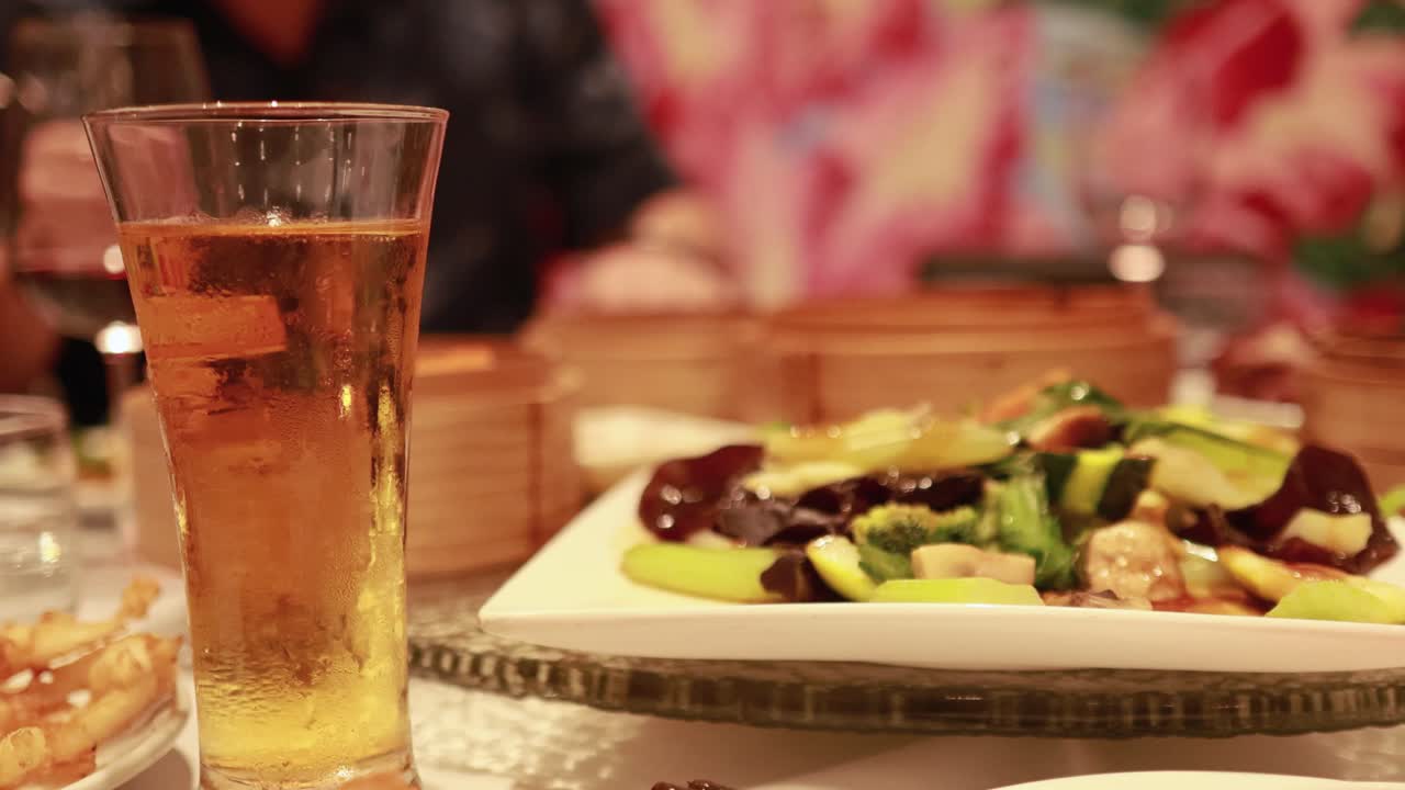 A lively restaurant scene with dim sum, colorful dishes, and a glass of beer on a table