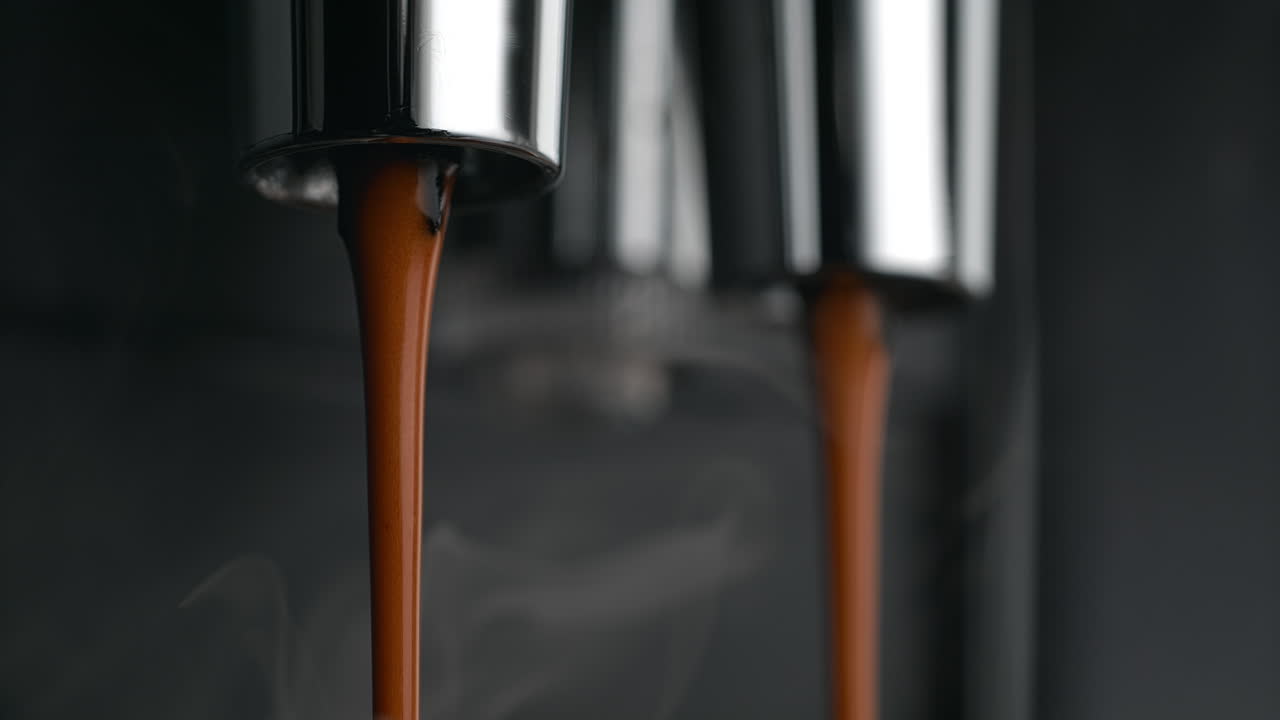 신선한 증기 커피가 에스프레소 머신의 이중 포타필터 스푸트에서 매크로와 느린 동작으로 흘러나옵니다.