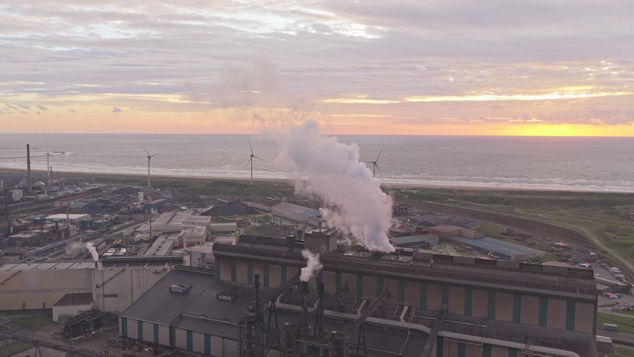 Bright sunset over heavy industry site with multiple chimneys smoking