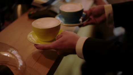 close up shot of a man taking his order of two cappuccinos inside a coffee shop