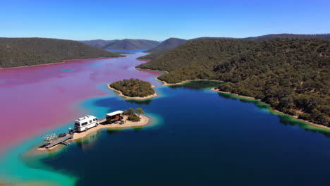 aerial view of an rv and cabin on a narrow strip of land between a vibrant pink lake and a blue lake