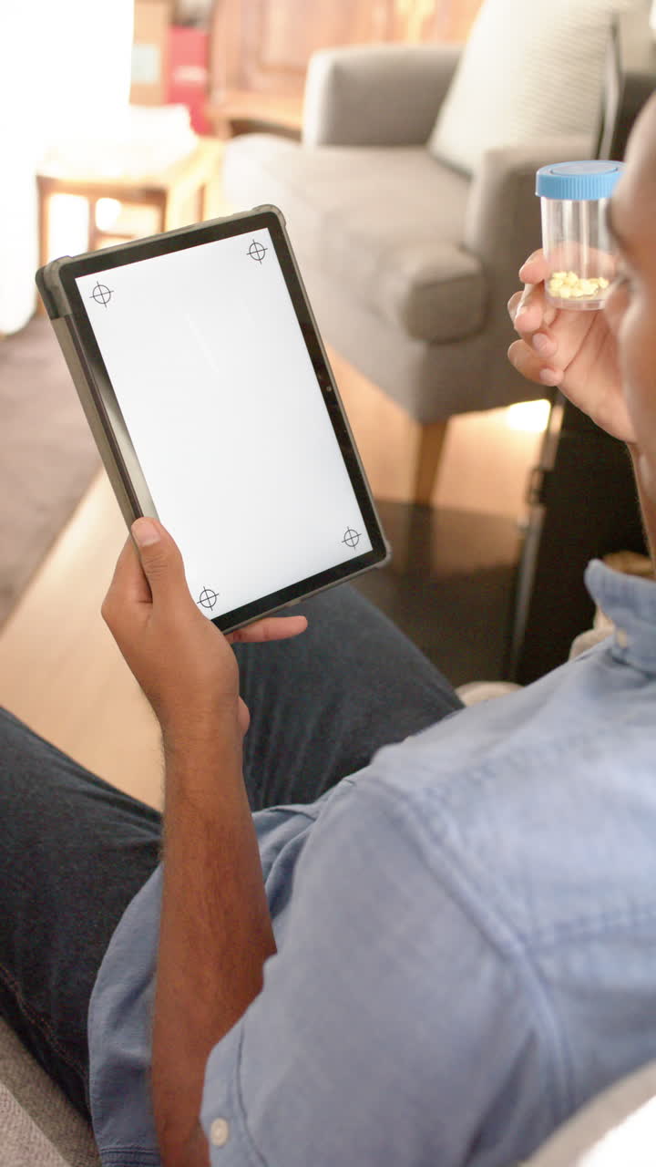 Vertical video of anglo indian man holding medication making video call using tablet, copy space